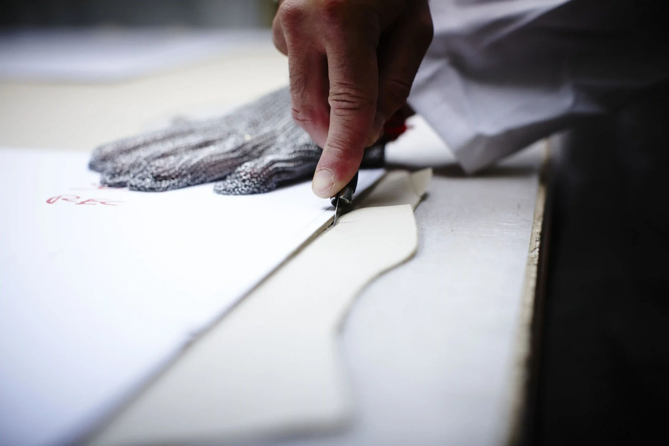 Mano che taglia la pelle con un taglierino seguendo una dima, mentre l&rsquo;altra mano indossa un guanto antitaglio per sicurezza